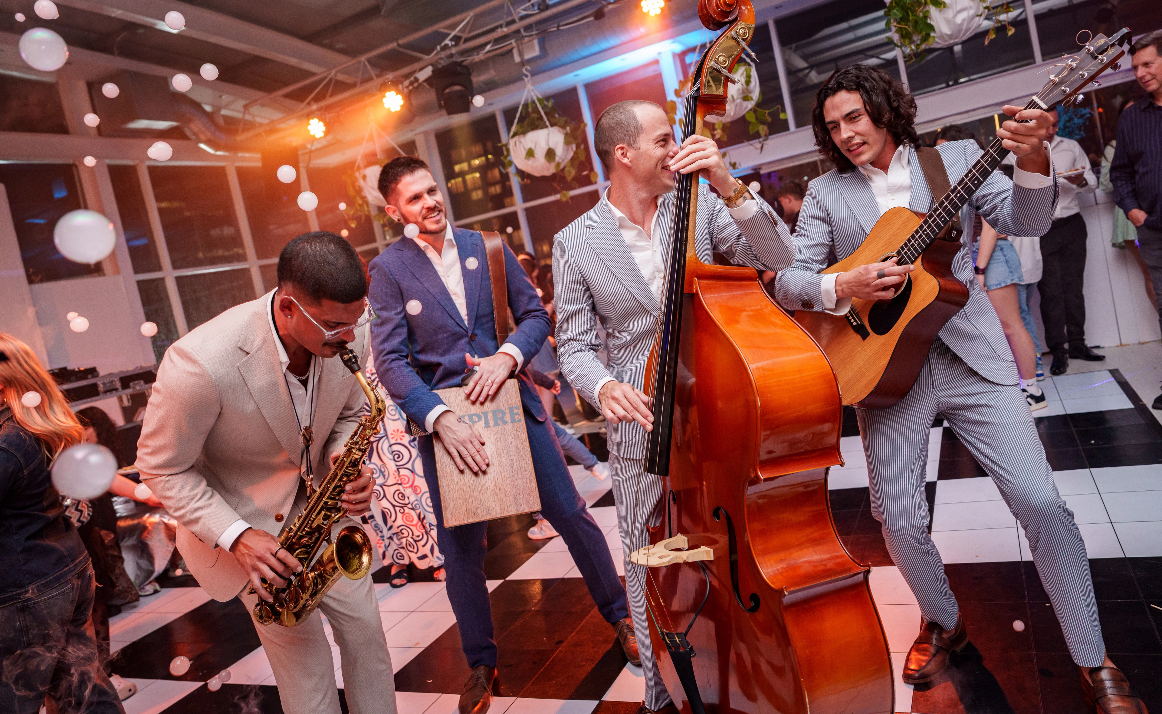 Empire musicians playing saxophone, cajón, double bass and guitar among guests at an evening event