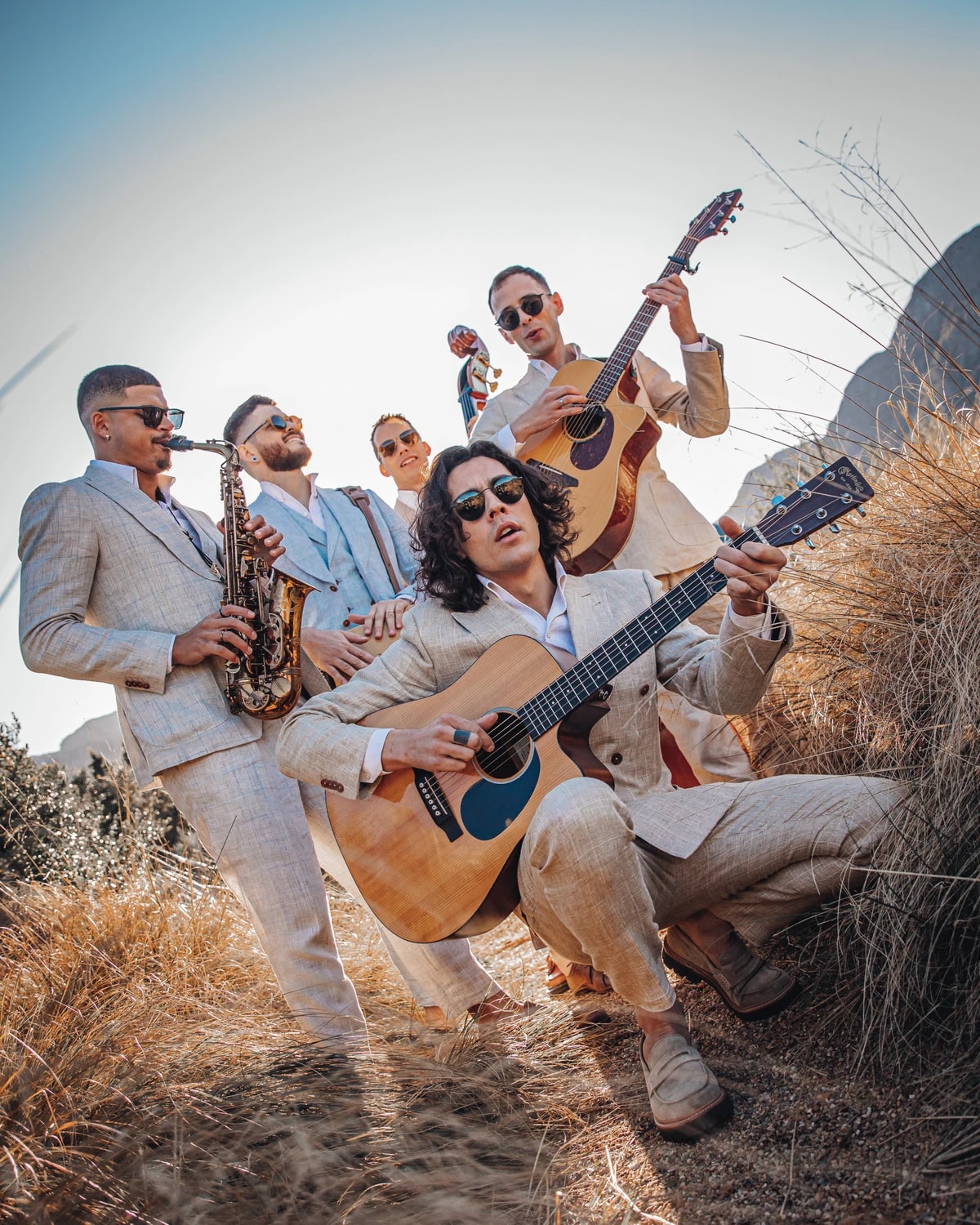 Five Empire musicians performing together on a mountain slope in light suits