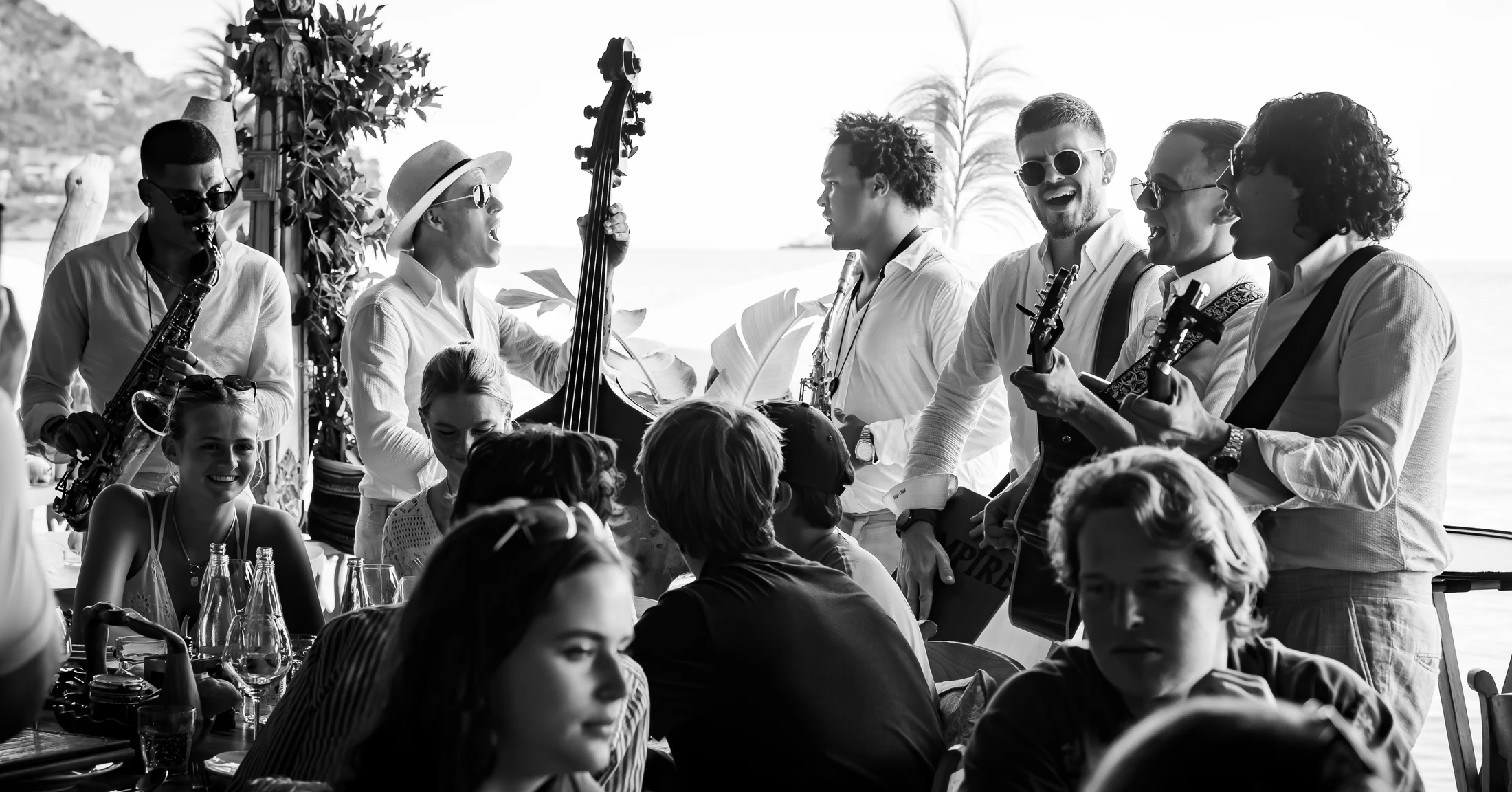 Empire musicians performing among seated guests at a seaside celebration in black and white